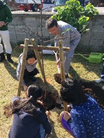 こども達と桜の苗木に土かけする沖縄出光沖縄油槽所　藤 浩和 所長