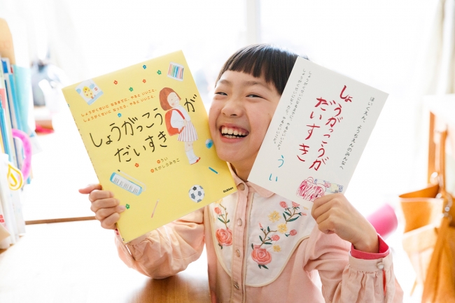 ▲作者のういさん。左手に持っているのが、本絵本の原本となった小冊子です。小学校生活を楽しく、もっと大好きになれるようにとのういさんの希望により、絵本とこの冊子をセットにしてプレゼントします！