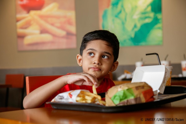 バングラデシュのファーストフード店でハンバーガーを頬張る男の子。(2019年9月13日撮影) © UNICEF_UNI210858_Sujan