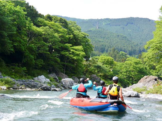 新緑の下、水しぶきを浴びて川を下るラフティング